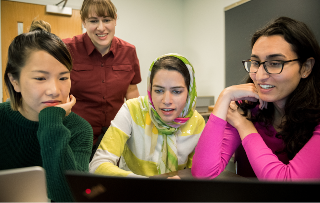 Picture of young women sitting together looking at a monitor while an instructor looks on